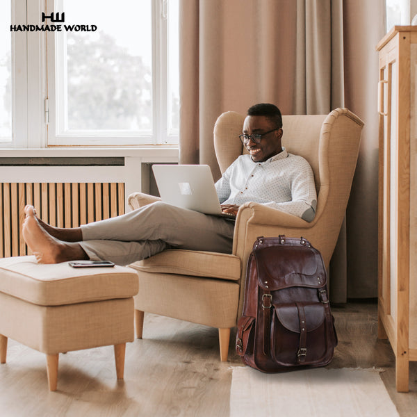Man sitting on sofa working on laptop and beside is leather laptop backpack By Handmade World